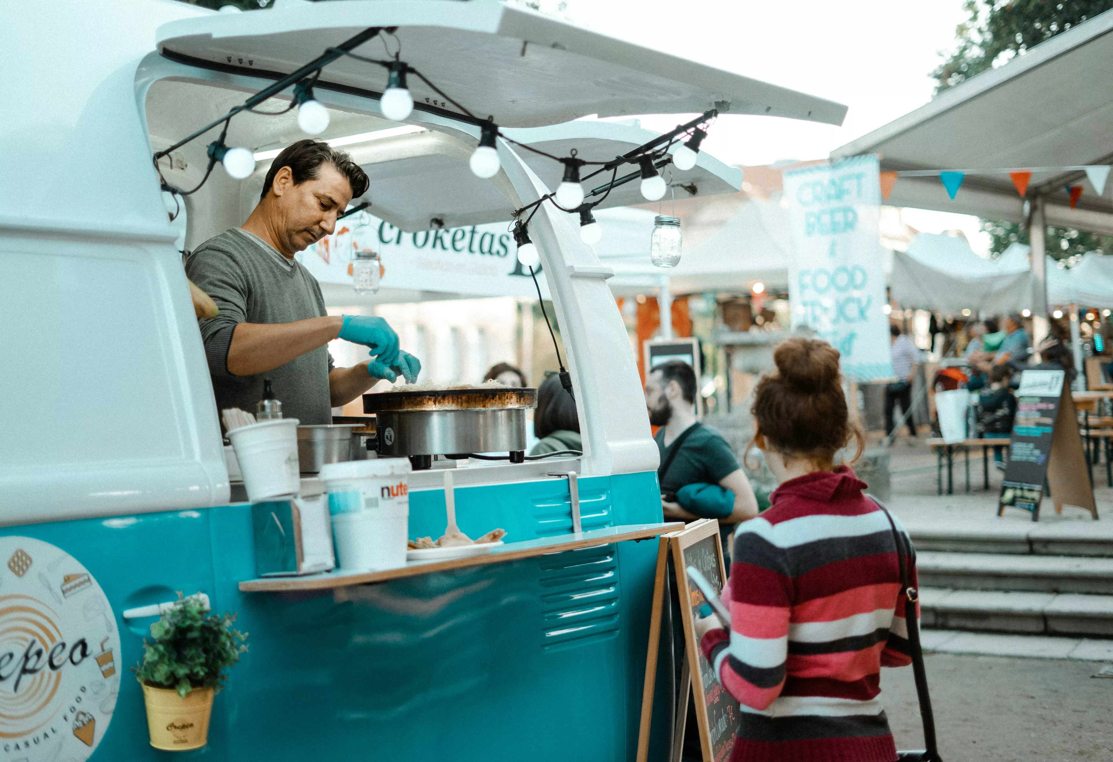 Una persona cocinando un crepe en un foodtruck y otra esperándo a su preparación